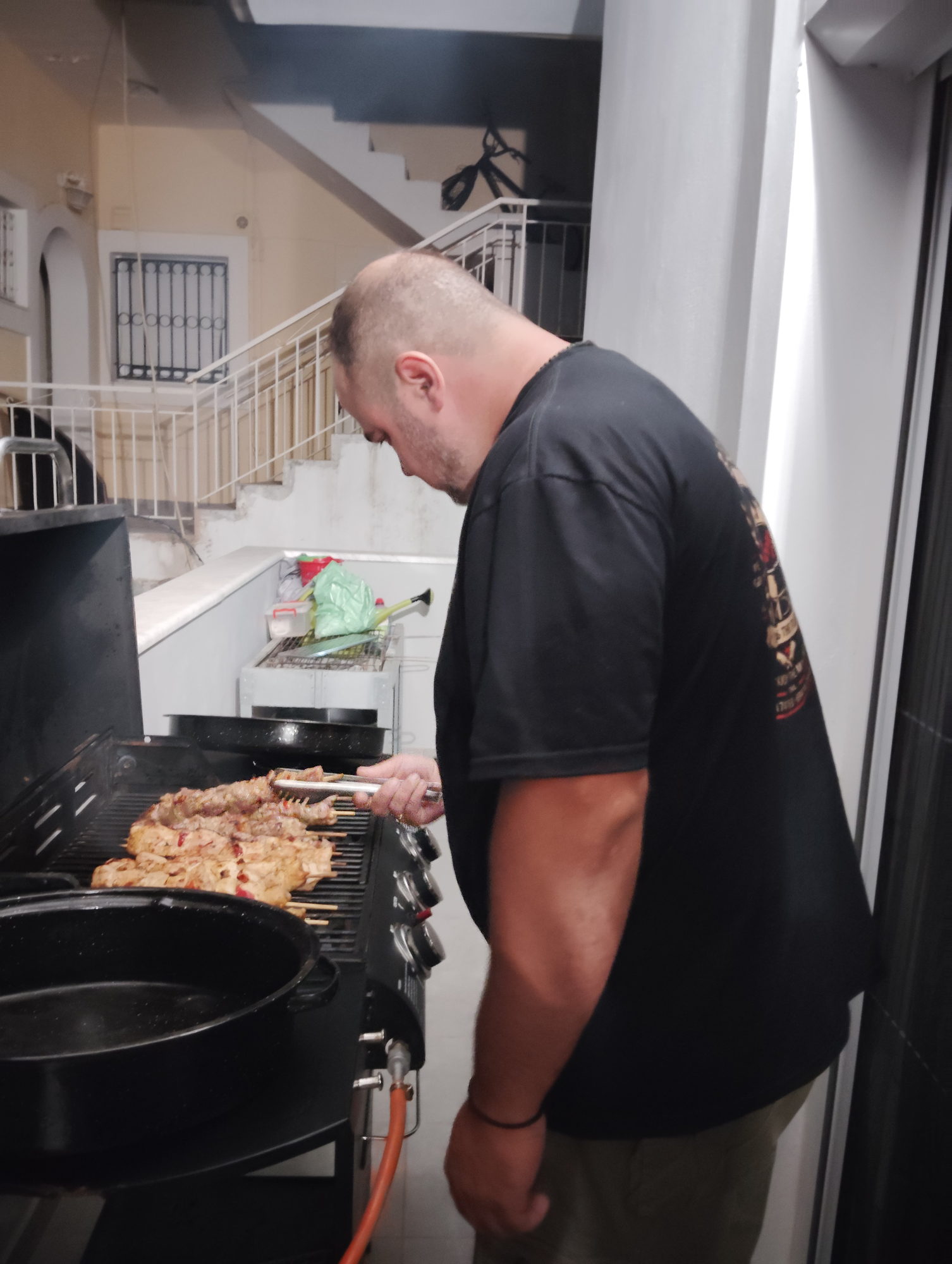 BBQ chef turning chicken souvlaki skewers on a gas grill during an evening service