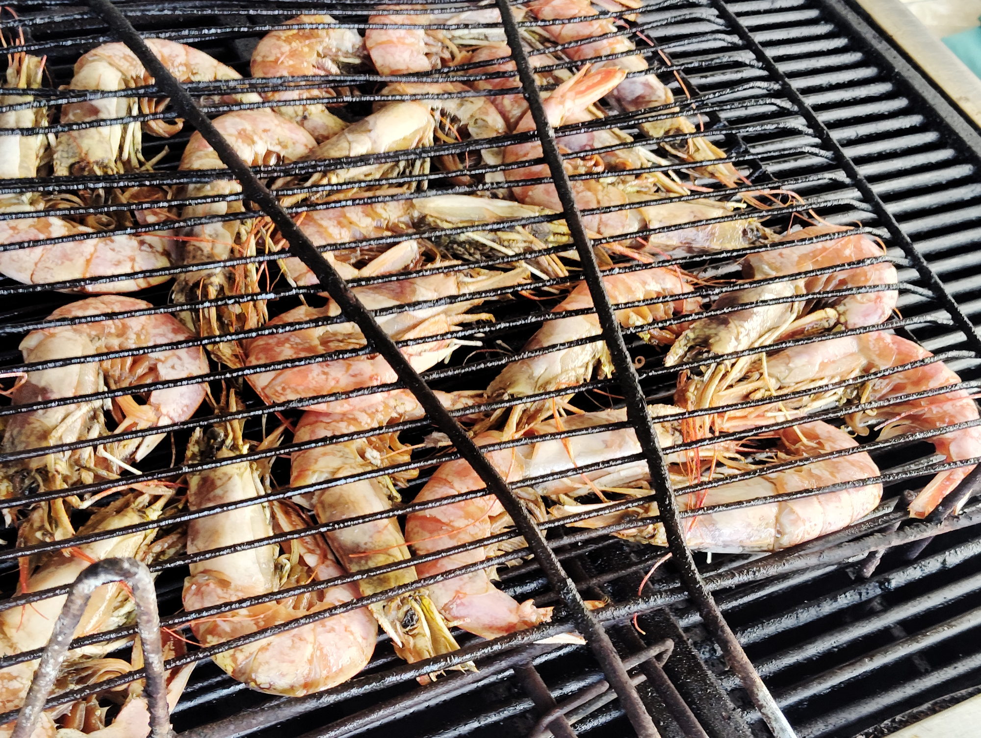 Large prawns grilling in a hinged wire basket over the coals