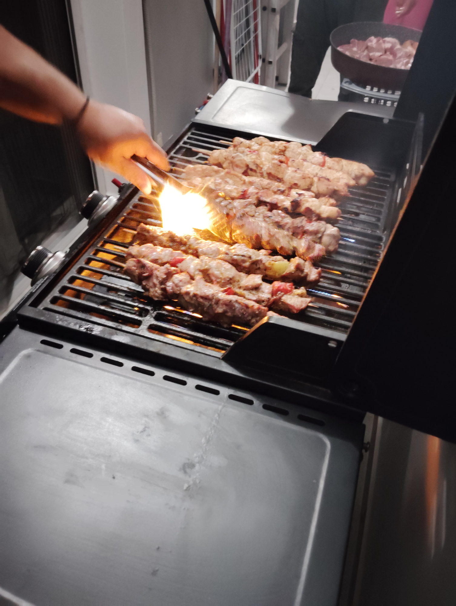 Flame rising beneath souvlaki skewers on a live fire grill