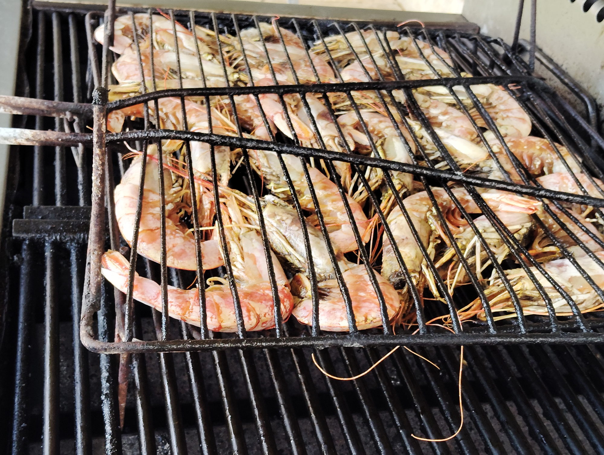 Prawn basket set over the grill bars, shells turning pink in the heat