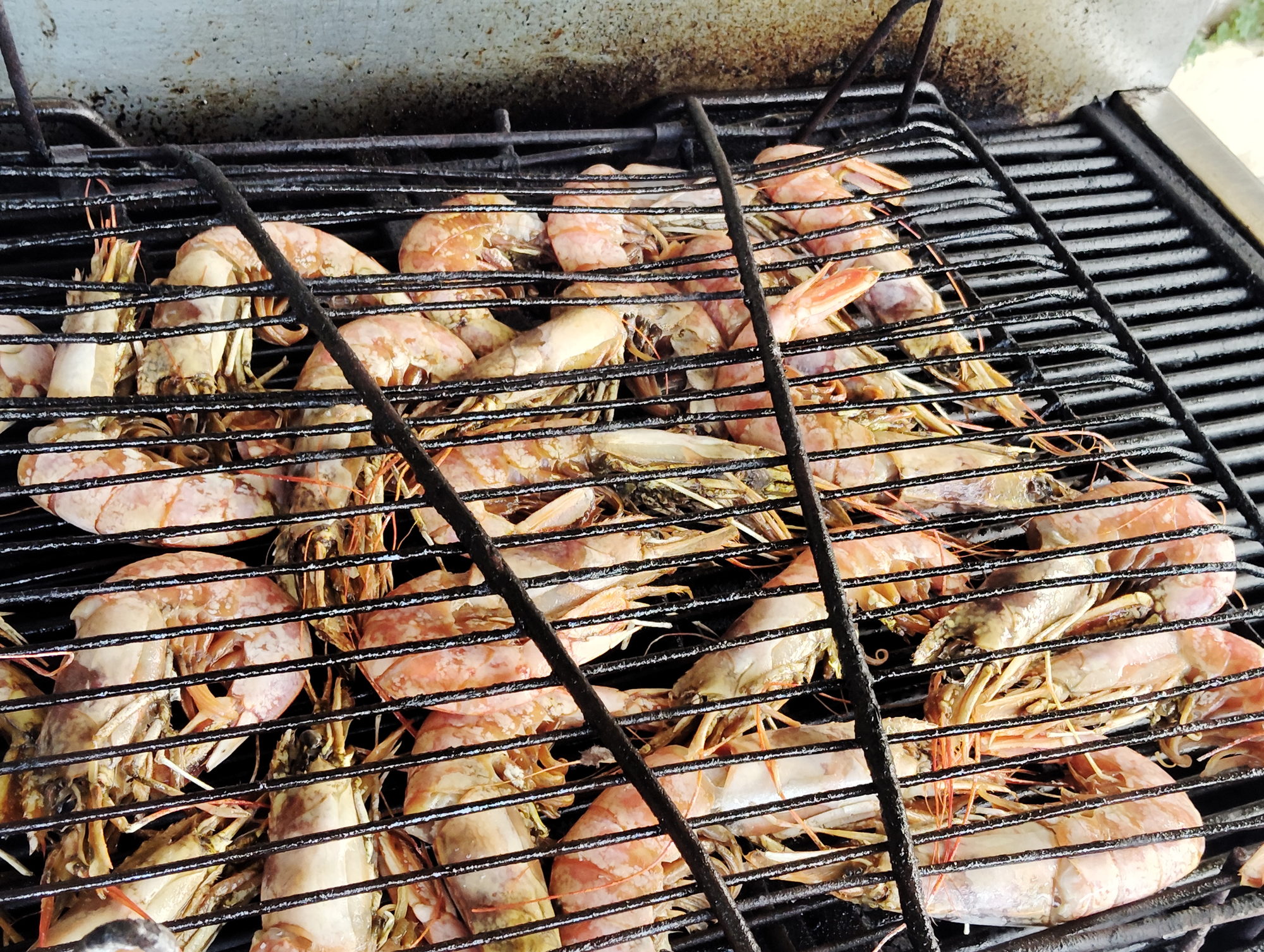 A full basket of prawns cooking across the width of the barbecue