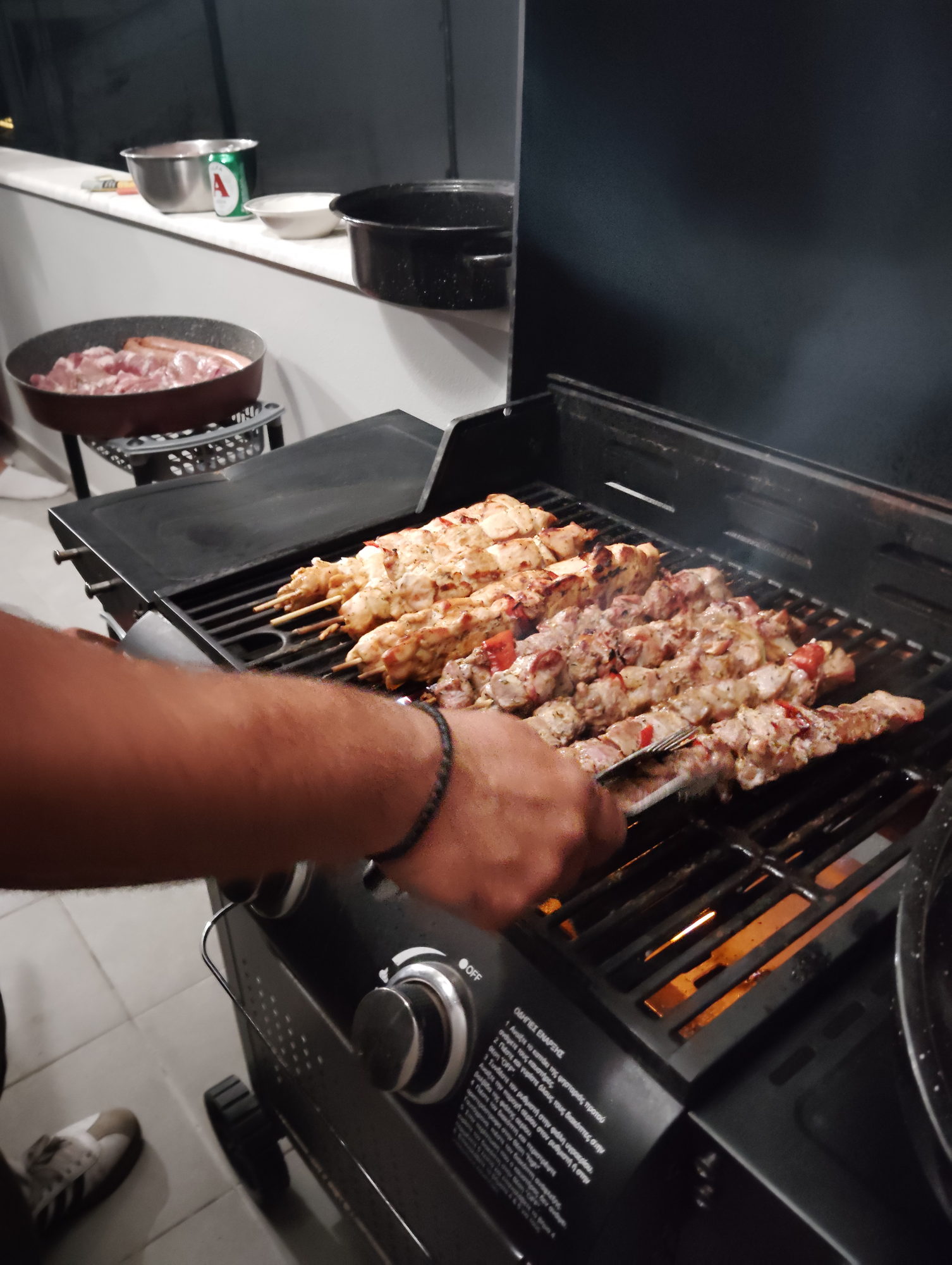 Souvlaki skewers being turned by hand on an outdoor barbecue in Corfu